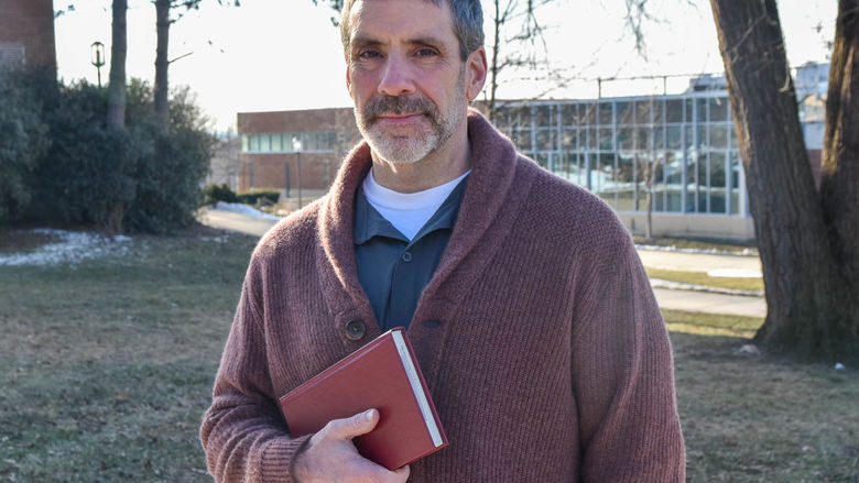 Bearded male standing outside holding abook