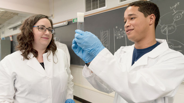 A student and professor examine a vial in a lab.