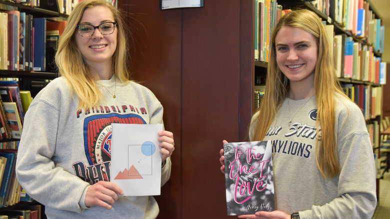 Female with long blood hair and glasses, left, holding a book, female with long blonde hair, right, holding a book.