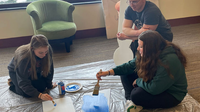 Two females and a male paint a giant letter K