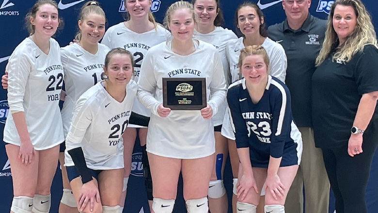 Eight female student-athletes iat Penn State York in volleyball uniforms and a female and male coach pose with award