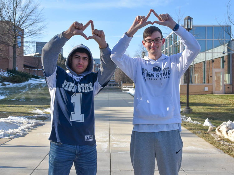 Two male students wearing Penn State attire and forming diamons with their hands