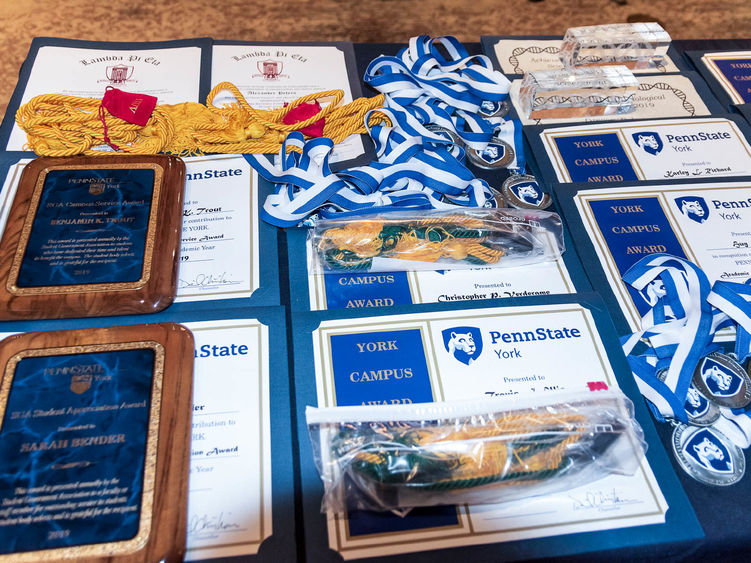 Award plaques, certificates and medals spread across a table at Penn State York. 