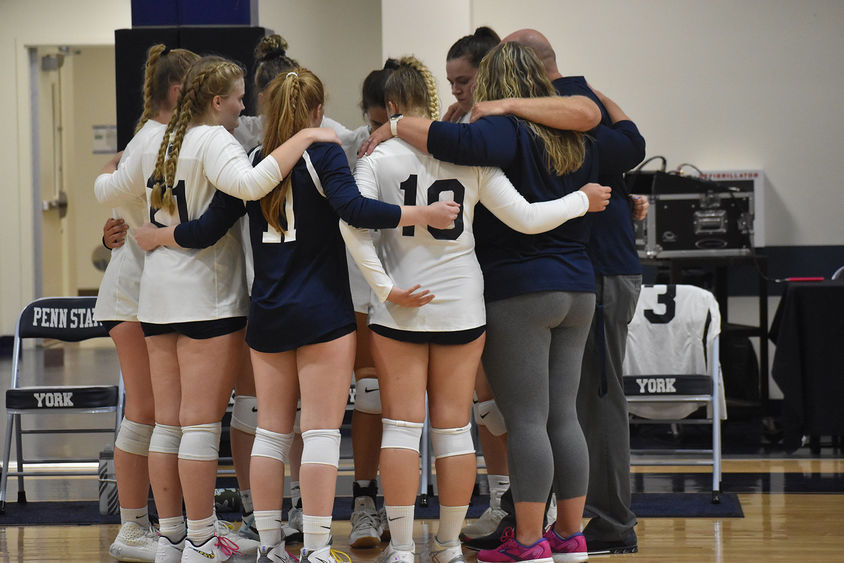Women's volleyball players and coaches in a huddle on the basketball court