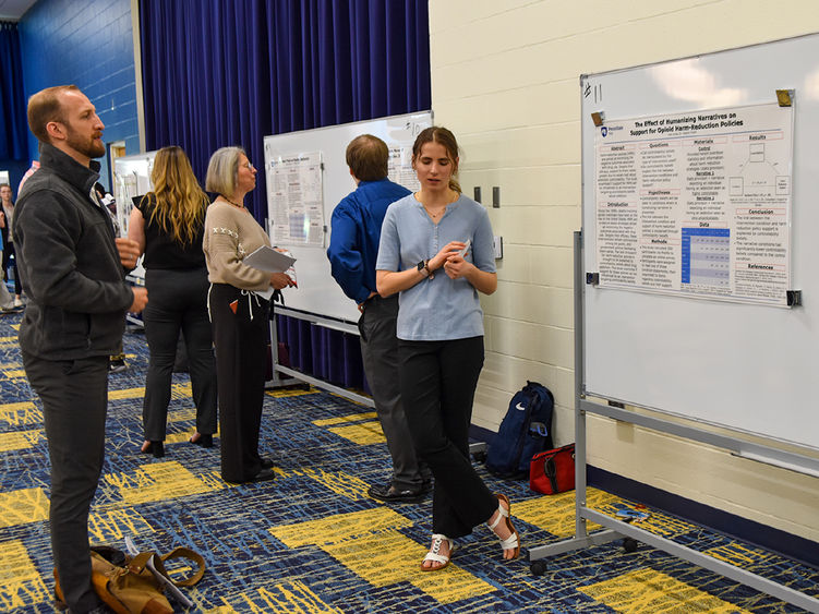 Research posters displayed on boards with students and faculty reviewing them
