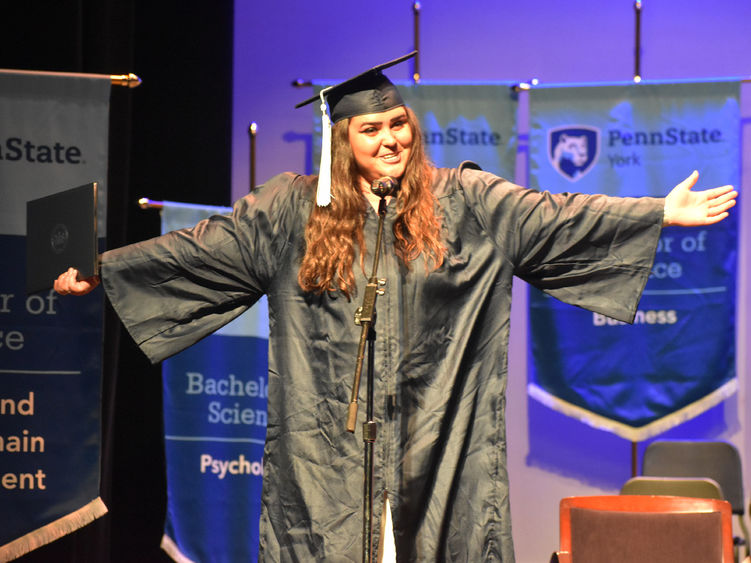 Female student in graduation cap and gown speaking at microphone