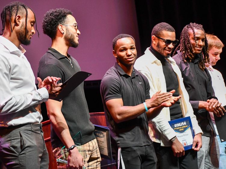 Young men stand in a line on a stage, some holding awards, some clapping.
