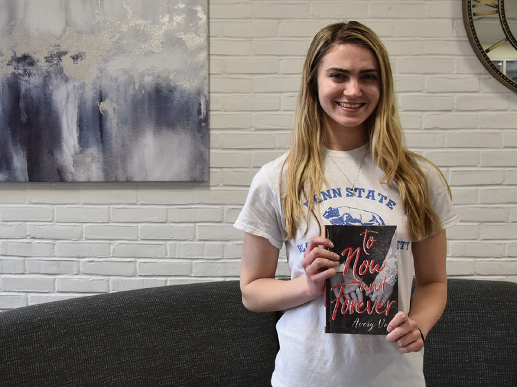 Young caucasian woman with long hair holding a book, art on the wall in the background.