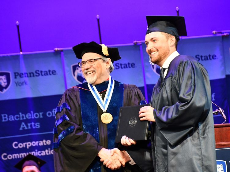 Two men in regalia shaking hands at a graduation ceremony.