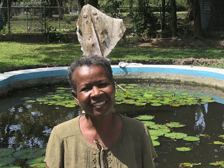 African American woman with short hair standing in front of a fountain of water and lily pads..