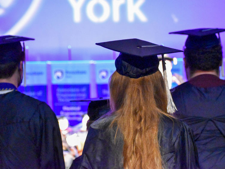 The back of students incommencement caps and gowns who are facing the stage