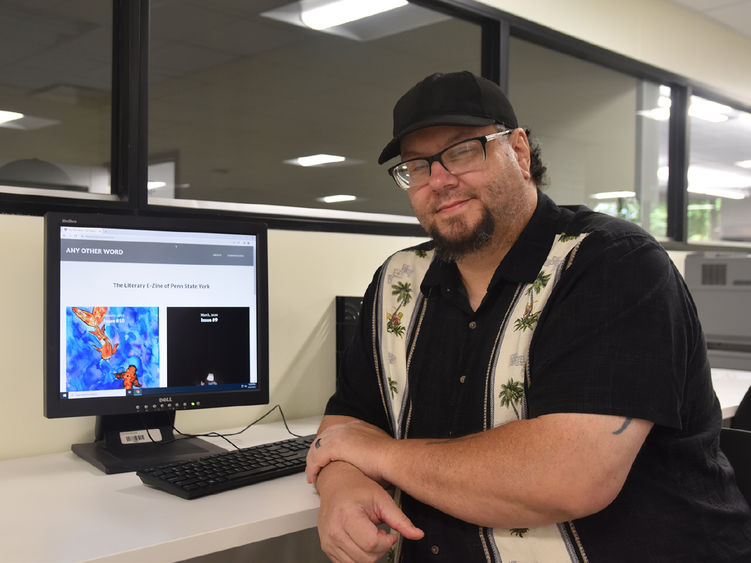 Adult student wearing glasses and a hot at a computer displays the campus online magazine.