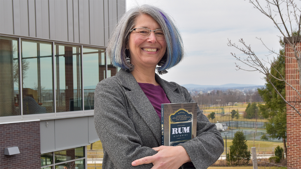 Female English faculty member holding her recently published book standing outside at Penn State York