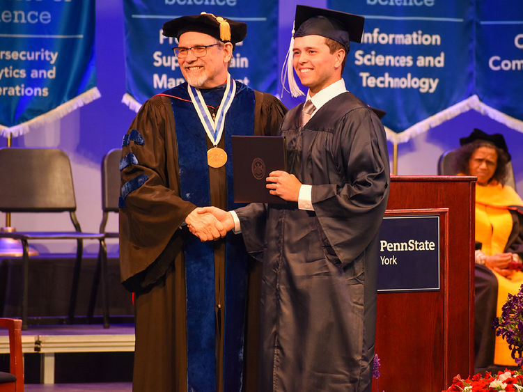 Older man and student in commencement regalia on stage shaking hands