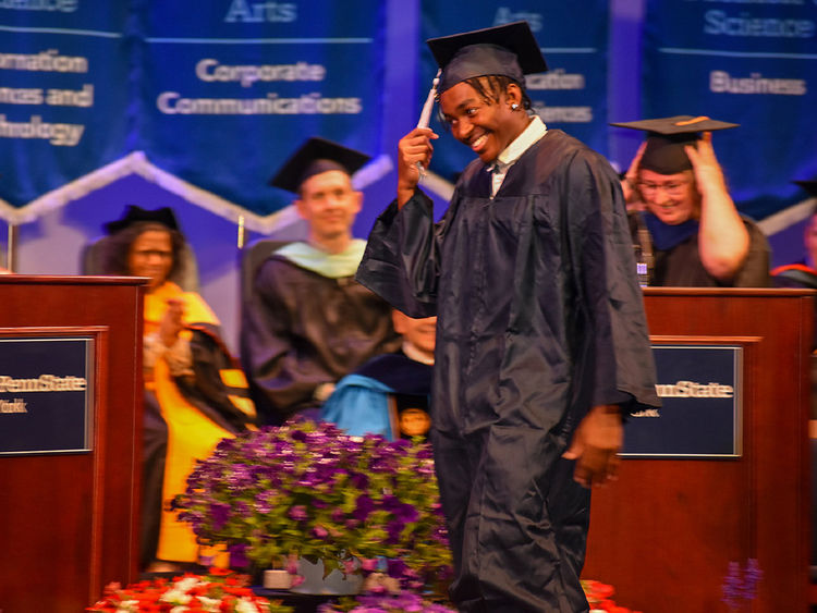 African American student in cap and gown crossing the stage and grabbing tassel at commencement