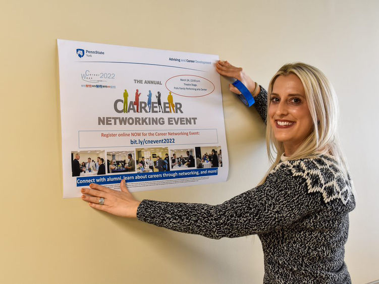 Feamale with long blonde hair hanging up poster concerning Career Week on campus