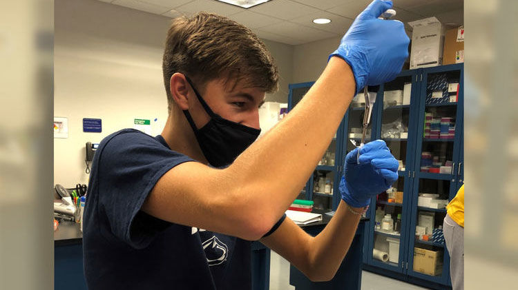 Male student wearing a facemask and working in a lab setting on undergraduate research.
