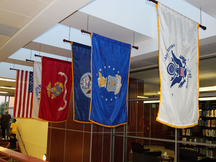 Military banners of several kinds are displayed alongside an American flag.