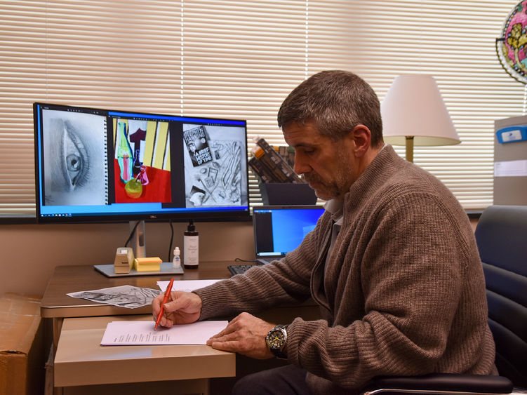 Man editing materials at a desk with visual art displayed on a computer screen