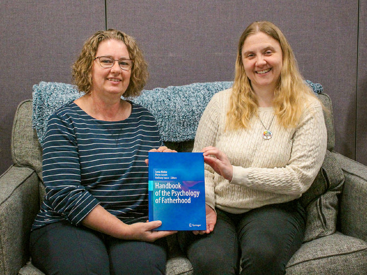 Two female faculty members sitting on a couch showing off their bool