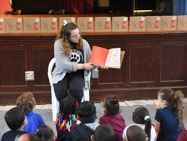 A Penn State York female student turns the pages of a book and reads to elementary school children.