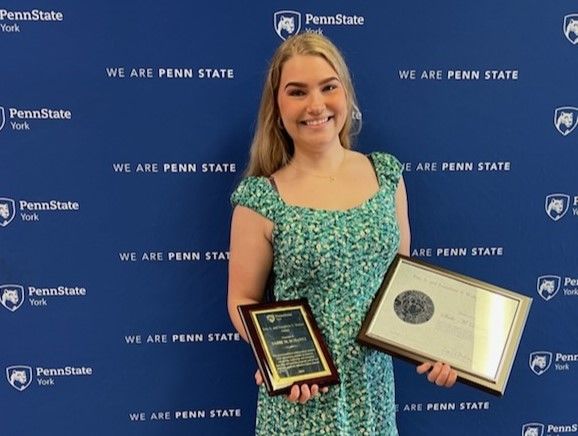 Person smiling, holding plaques, standing in front of blue backdrop.