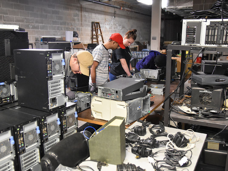 Group of students working  on computers and other electronics with pieces of equipment around the room