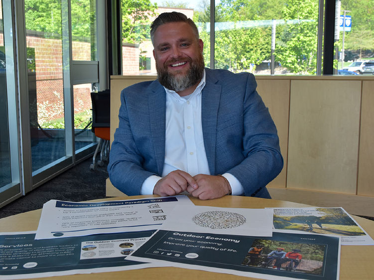 Bearded white male dressed in a suit showing off materials on the desk in front of him.