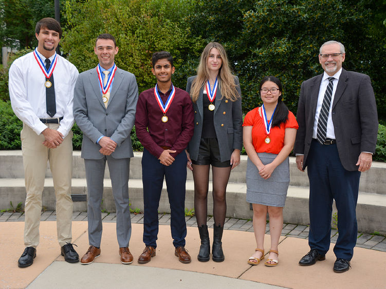 Three male and two female students pose with older gentleman wearing glasses