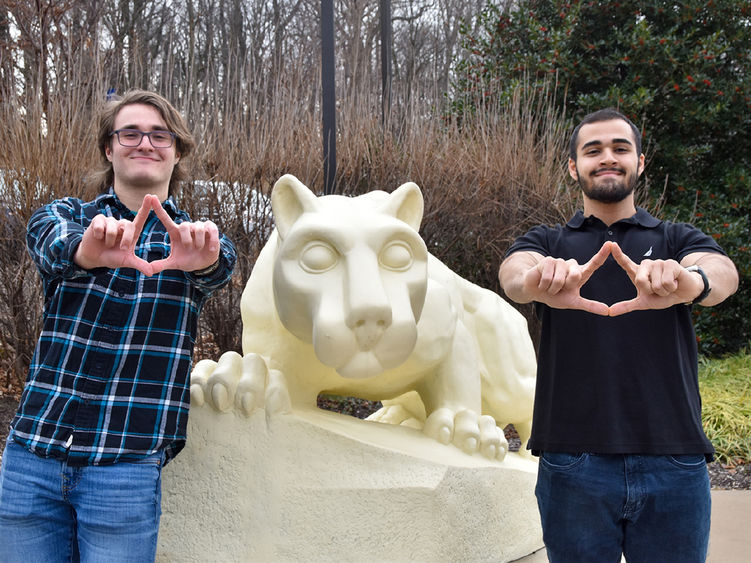 Two males flank the Nittany Lion Shrine at Penn State York and make a diamond shape with their fingers.