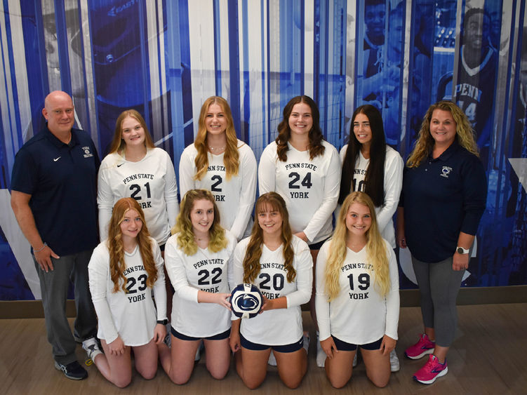 Eight femal volleyball players, dressed in uniform, and a male and female coach.